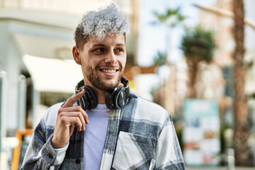 Young hispanic man smiling happy using headphones at the city.