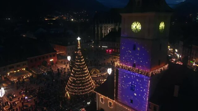 Aerial drone view of The Council Square in Brasov at night, Romania. Old city centre decorated for Christmas. County Museum of History, buildings, people