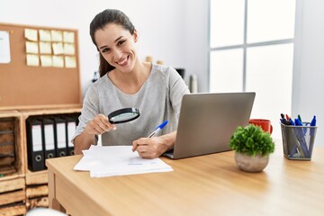 Young hispanic woman using magnifying glass working at office