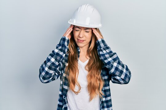 Young caucasian woman wearing architect hardhat suffering from headache desperate and stressed because pain and migraine. hands on head.