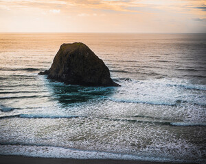 Haystack rock along the coastline, riding waves into the sunset