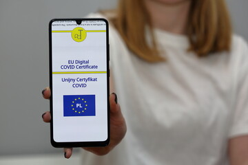 woman holding a mobile phone with EU Digital Covid Certificate and flag of European Union and leterrs PL inside