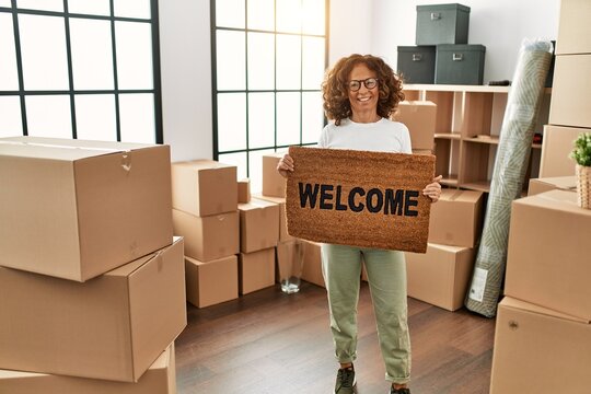 Middle Age Hispanic Woman Smiling Confident Holding Welcome Doormat At New Home