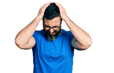 Fototapeta premium Hispanic man with beard wearing casual t shirt and glasses suffering from headache desperate and stressed because pain and migraine. hands on head.