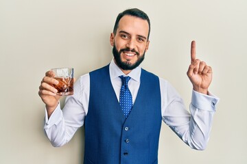 Young man with beard drinking whiskey shot surprised with an idea or question pointing finger with happy face, number one