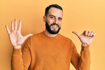 Young man with beard wearing casual winter sweater showing and pointing up with fingers number six...