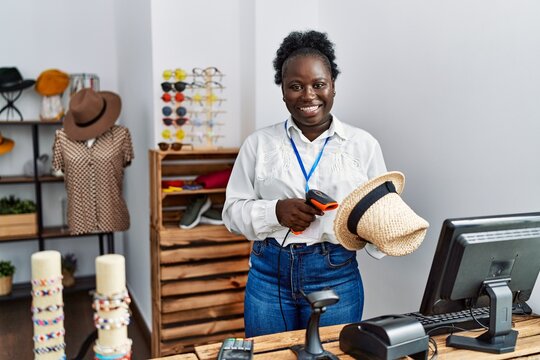 Young african american woman shopkeeper scanning hat using barcode reader at clothing store