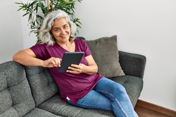 Obraz premium Middle age grey-haired woman using touchpad sitting on the sofa at home.