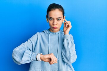 Young caucasian blonde woman using earphones and smart watch skeptic and nervous, frowning upset because of problem. negative person.