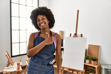 Young african american woman with afro hair at art studio cheerful with a smile on face pointing...