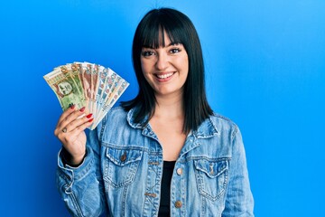 Young hispanic woman holding peruvian sol banknotes looking positive and happy standing and smiling...
