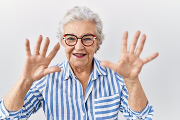 Senior woman with grey hair standing over white background showing and pointing up with fingers number ten while smiling confident and happy.