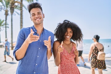 Young interracial couple outdoors on a sunny day pointing fingers to camera with happy and funny face. good energy and vibes.