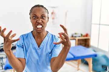 Black woman with braids working at pain recovery clinic shouting frustrated with rage, hands trying...
