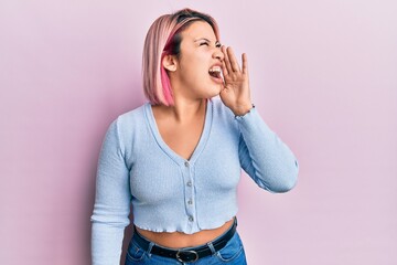 Hispanic woman with pink hair standing over pink background shouting and screaming loud to side with hand on mouth. communication concept.