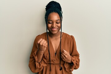 African american woman with braided hair wearing casual brown shirt celebrating surprised and amazed for success with arms raised and eyes closed