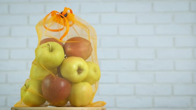 Reusable bag with fruits. A view of a reusable mesh bag with colorful ripe apples on the table.
