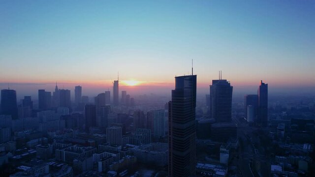 Morning flight over Warsaw. Aerial sunrise and fog oover Warsaw downtown skyline with skyscrapers, Poland. Reflections of the sun in the glass of a skyscraper