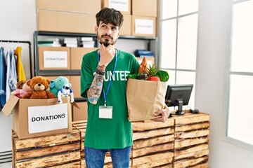 Hispanic man with beard wearing volunteer t shirt at donations point serious face thinking about...