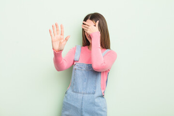 pretty young woman covering face with hand and putting other hand up front to stop camera, refusing...