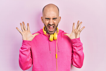 Young bald man wearing gym clothes and using headphones celebrating mad and crazy for success with...