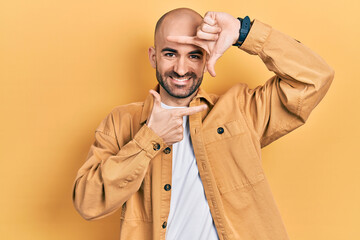 Young bald man wearing casual clothes smiling making frame with hands and fingers with happy face. creativity and photography concept.