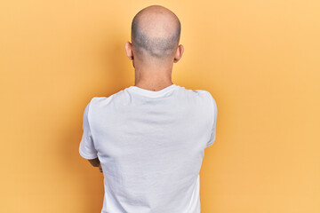 Young bald man wearing casual white t shirt standing backwards looking away with crossed arms