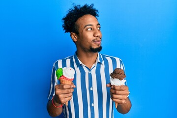 Young african american man with beard holding two ice cream cones smiling looking to the side and...