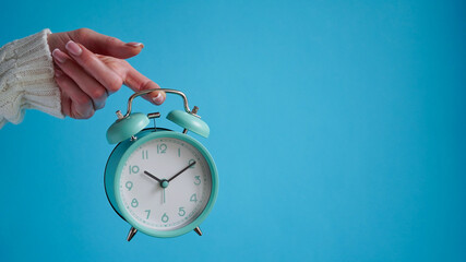 Close-up of woman's hand holding blue retro alarm clock blue background,time on clock is ten o'clock ten minutes,10:10.Time to wake up,early morning.Blue monday day concept.Copy space.Turquoise clock.