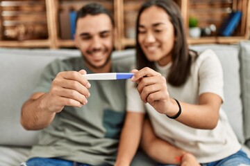 Young latin couple smiling happy looking pregnant test result at home.
