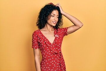 Young latin girl wearing summer dress smiling confident touching hair with hand up gesture, posing attractive and fashionable