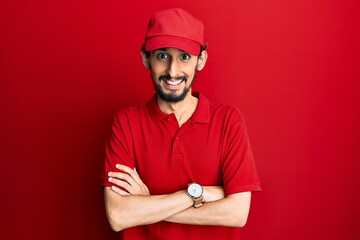 Young hispanic man wearing delivery uniform and cap happy face smiling with crossed arms looking at the camera. positive person.