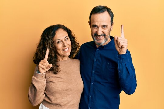 Middle age hispanic couple wearing casual clothes pointing finger up with successful idea. exited and happy. number one.