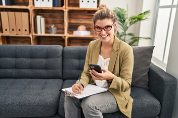 Obraz premium Young blonde woman psychologist using smartphone sitting on sofa at psychology center