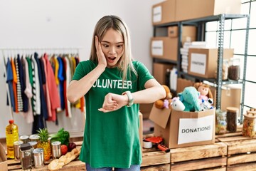 Asian young woman wearing volunteer t shirt at donations stand looking at the watch time worried, afraid of getting late