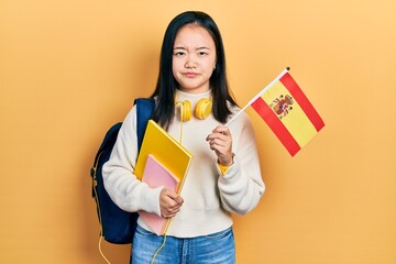 Young chinese girl exchange student holding spanish flag skeptic and nervous, frowning upset because of problem. negative person.