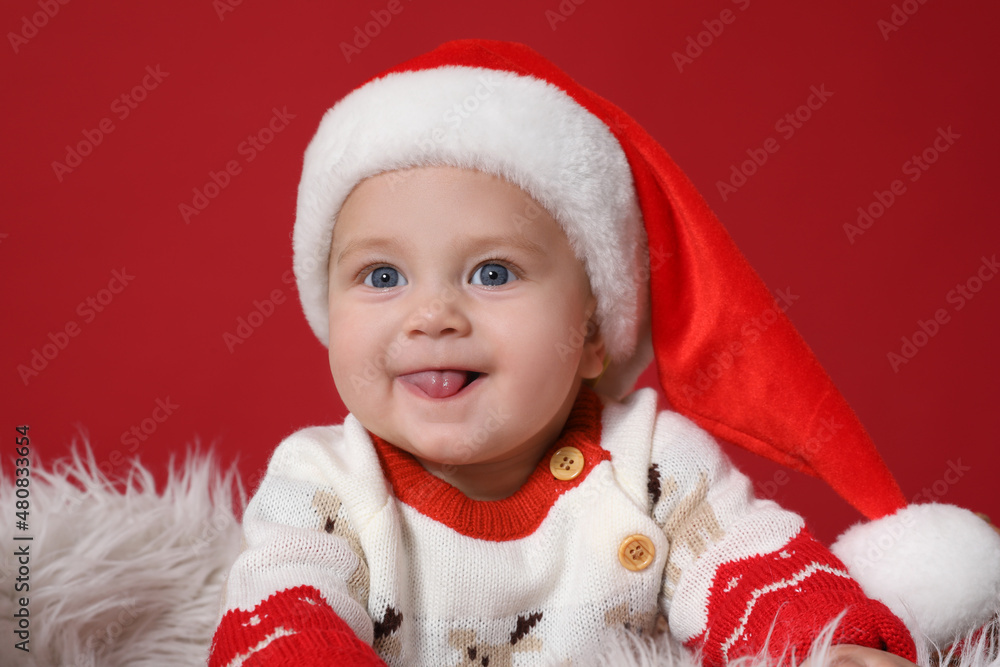 Wall mural Cute baby in Santa hat on red background. Christmas celebration