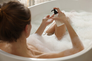 Beautiful woman pouring shower gel onto hand in bath indoors, focus on hands