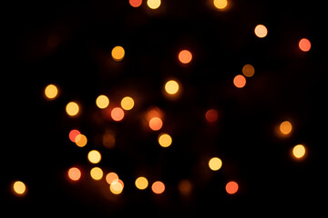 Defocused bokeh lights on black background, an abstract naturally blurred backdrop for Valentine's Day or birthday party. Festive light texture. Pink and red garland in blur. Overlay effect for design