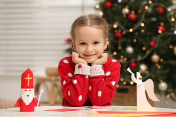 Cute little girl with paper Saint Nicholas and angel toys at home