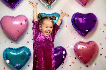 Little girl in a purple velvet dress throws confetti with great joy laughing with delight. Bright...