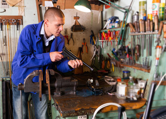 Portrait of concentrated skilled craftsman of weapons workshop engaged in repairing of small-bore handgun.