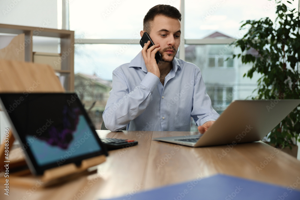 Poster forex trader talking on phone while working with laptop in office