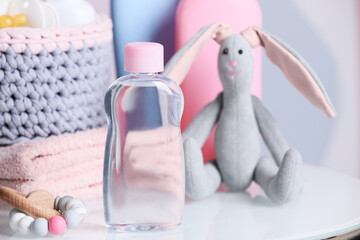 Bottle of baby cosmetic product, toys and accessories on white table against color background. Space for text