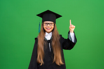 A schoolgirl dreams of entering a master's degree, a student points up at an advertisement, a cute girl in a master's gown on a green isolated background. the child graduated from high school.