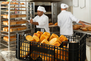 Fresh crispy bread in plastic crate in professional kitchen, working day at bakery