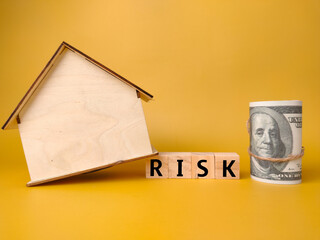 Wooden house,banknotes and wooden block with word RISK on yellow background.