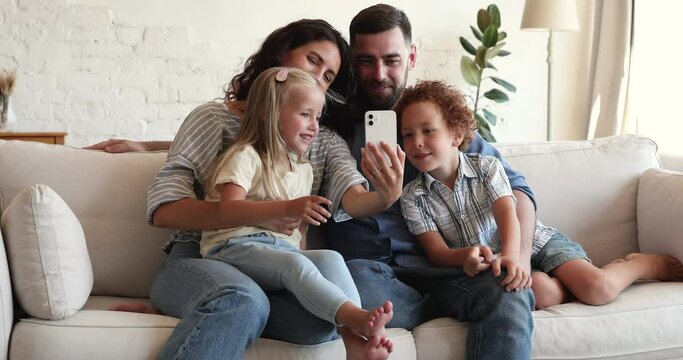 Beautiful family with little siblings relaxing on couch have fun use wireless technology, entertaining take selfie pictures or make video call, enjoy new mobile app spend leisure at home. Tech concept