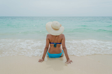 Fototapeta na wymiar Espalda de mujer en traje de baño posando sentada en Playa Blanca Barú en Cartagena en Colombia