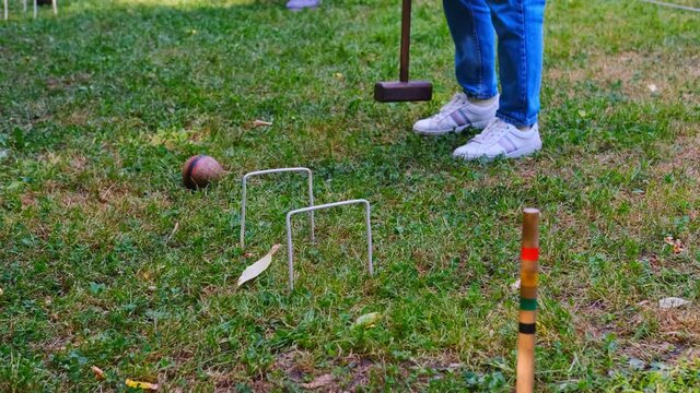 Person plays a sports game of croquet on a green field strike mallets on a ball and conducts through hoops. 